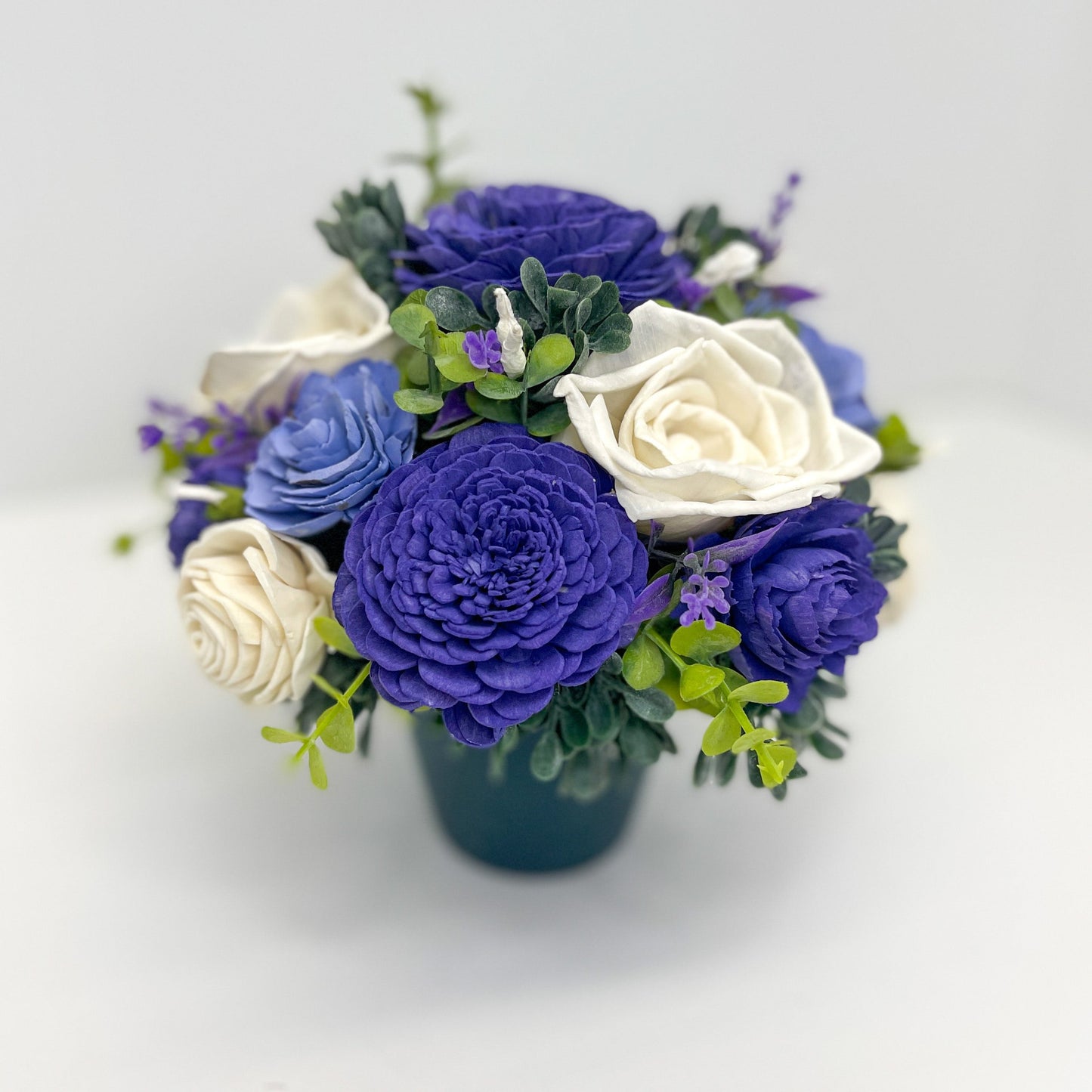 Dark purple, light purple & white wooden flower bouquet with greenery placed in planter.