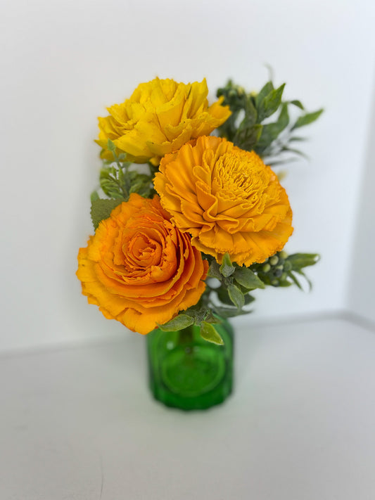 Orange flower bouquet with greenery placed in green, translucent vase. 