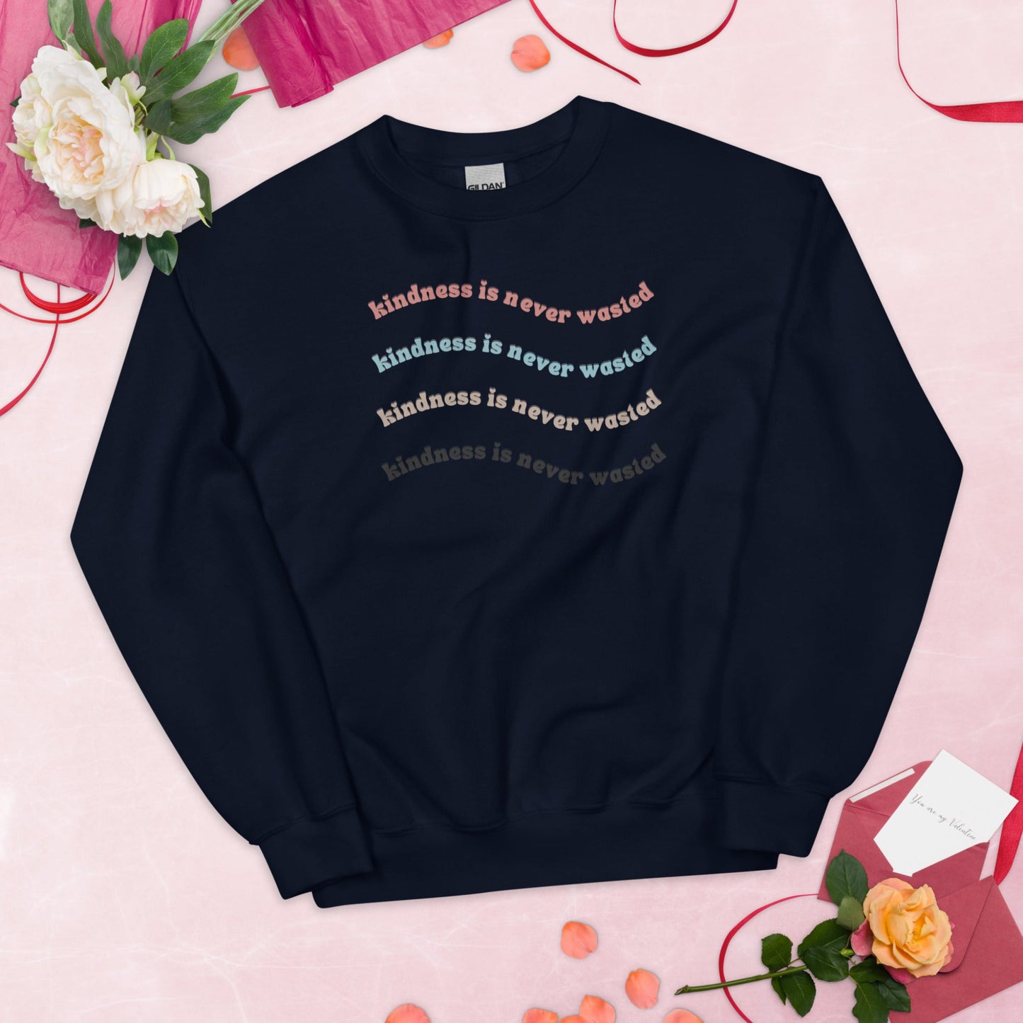 Navy "kindness is never wasted" crew neck with print in pink, yellow, light blue, and grey.