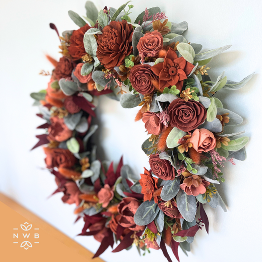 Burnt orange and pink handcrafted wooden floral wreath with greenery. 