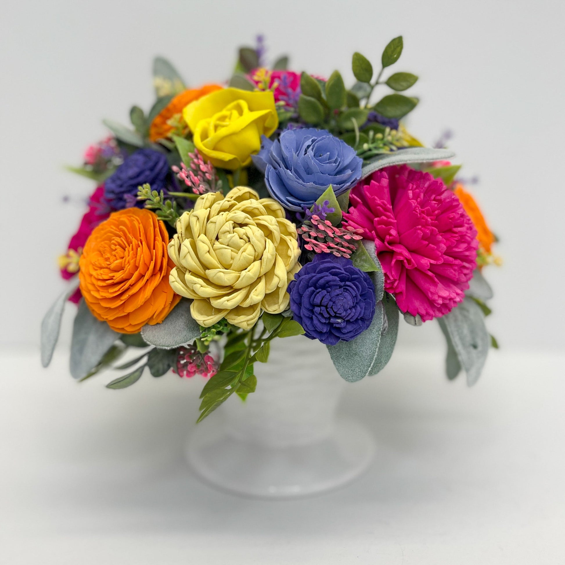 Bright and cheery handcrafted bouquet with blue, pink, purple, and orange florals in a while vase. 