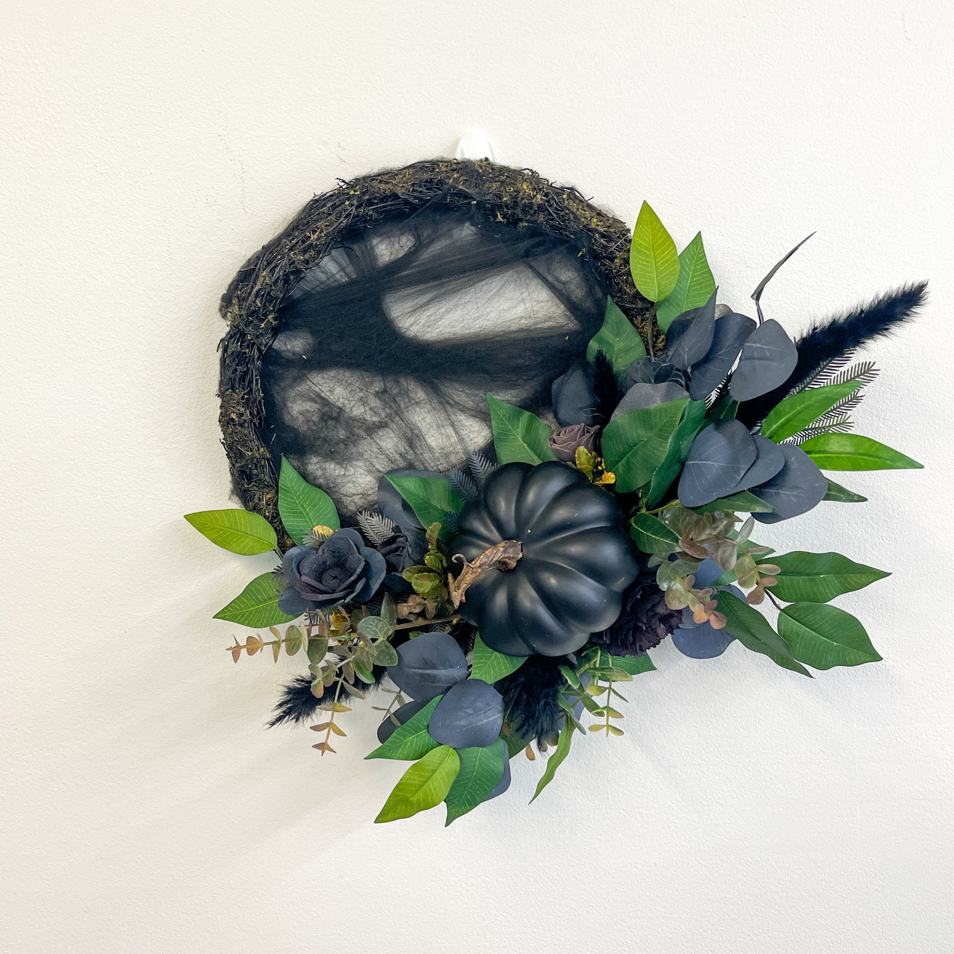 Black wooden flower wreath with black cobwebs. flowers, pumpkin and incorporated greenery.