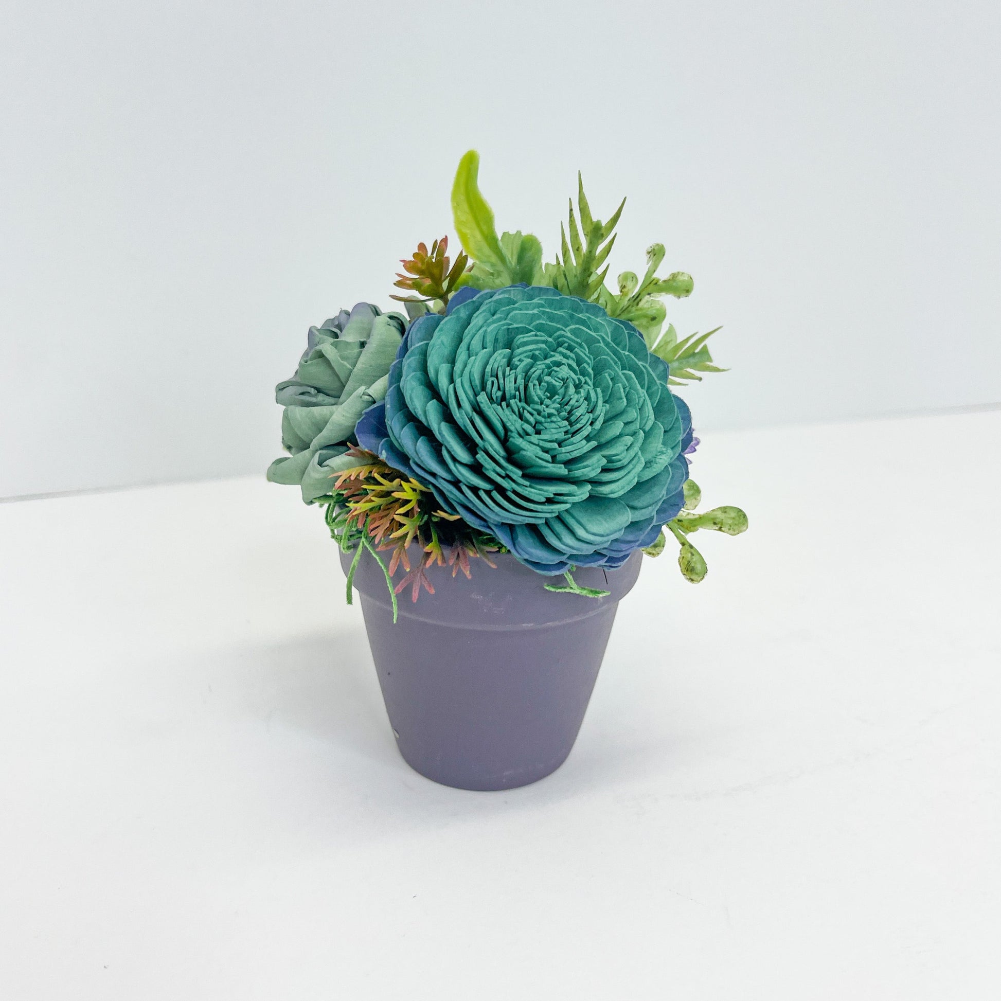 Blue and green wooden succulent with greenery placed in a painted purple pot.