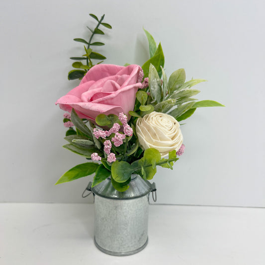 Light pink and white rose flower bouquet with greenery placed in silver mini milk can vase .