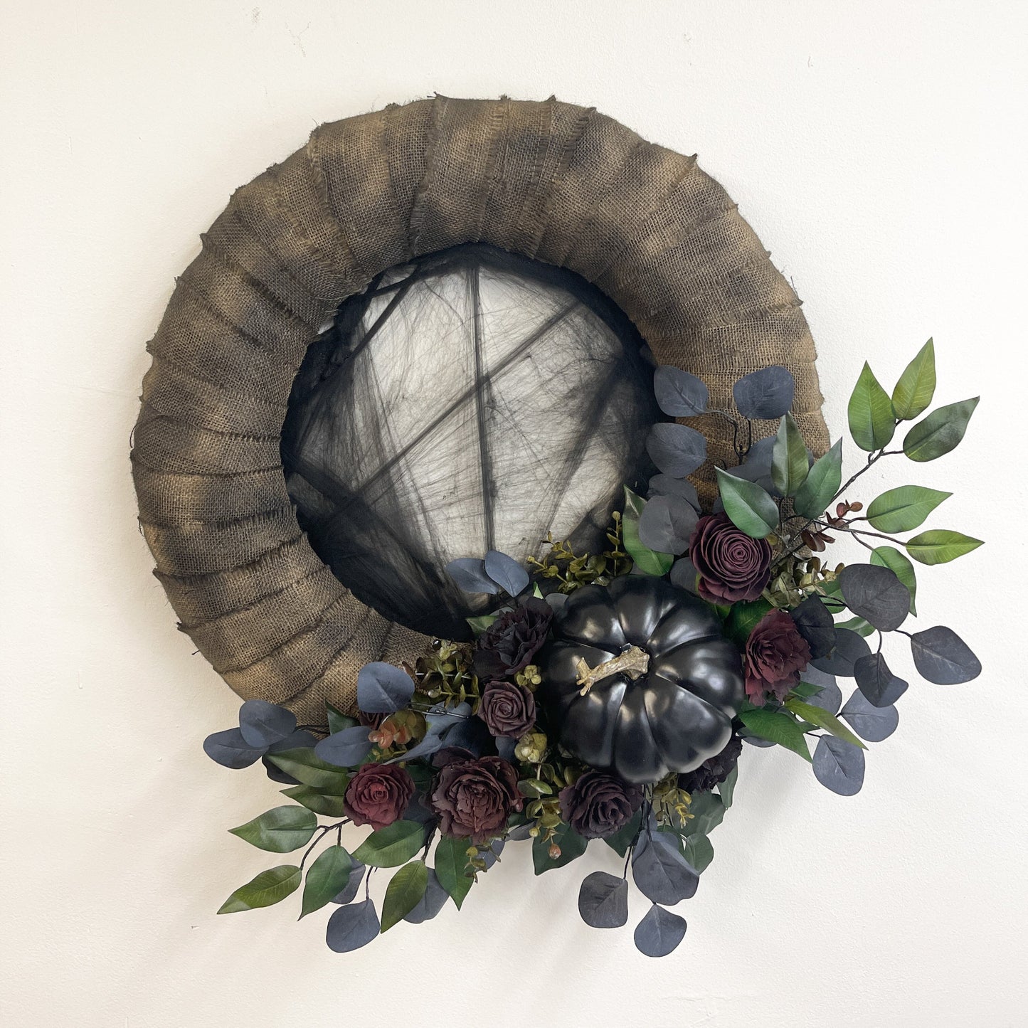 Wood flower wreath with black cobwebs, maroon flowers, black pumpkin, and black and green greenery.
