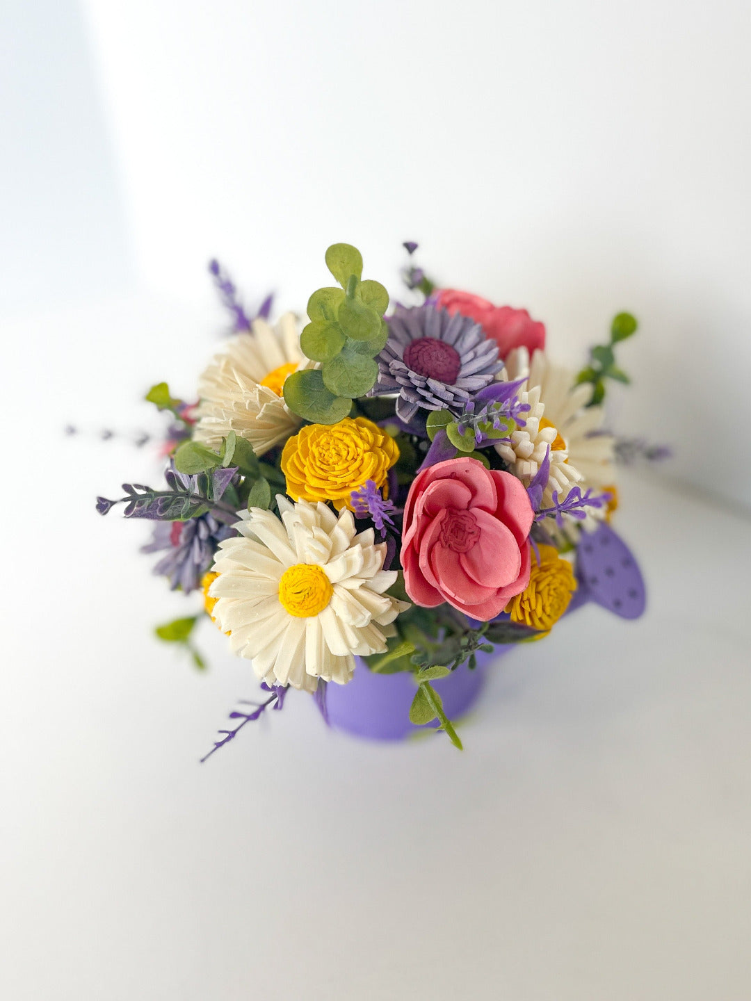 Mini purple watering can pair with white, pink, yellow, purple, and greenery wooden floral bouquet. 