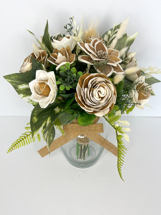 Ivory and tan handcraften wooden flower bouquet with greenery placed in clear vase with tan bow. 