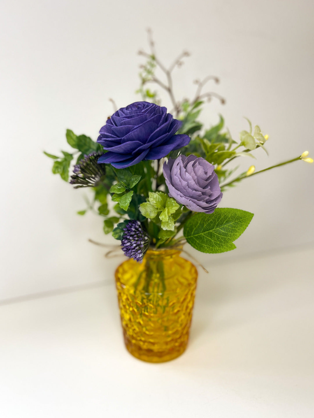 Dark purple & light purple wooden flower bouquet with greenery placed in yellow bud vase. 