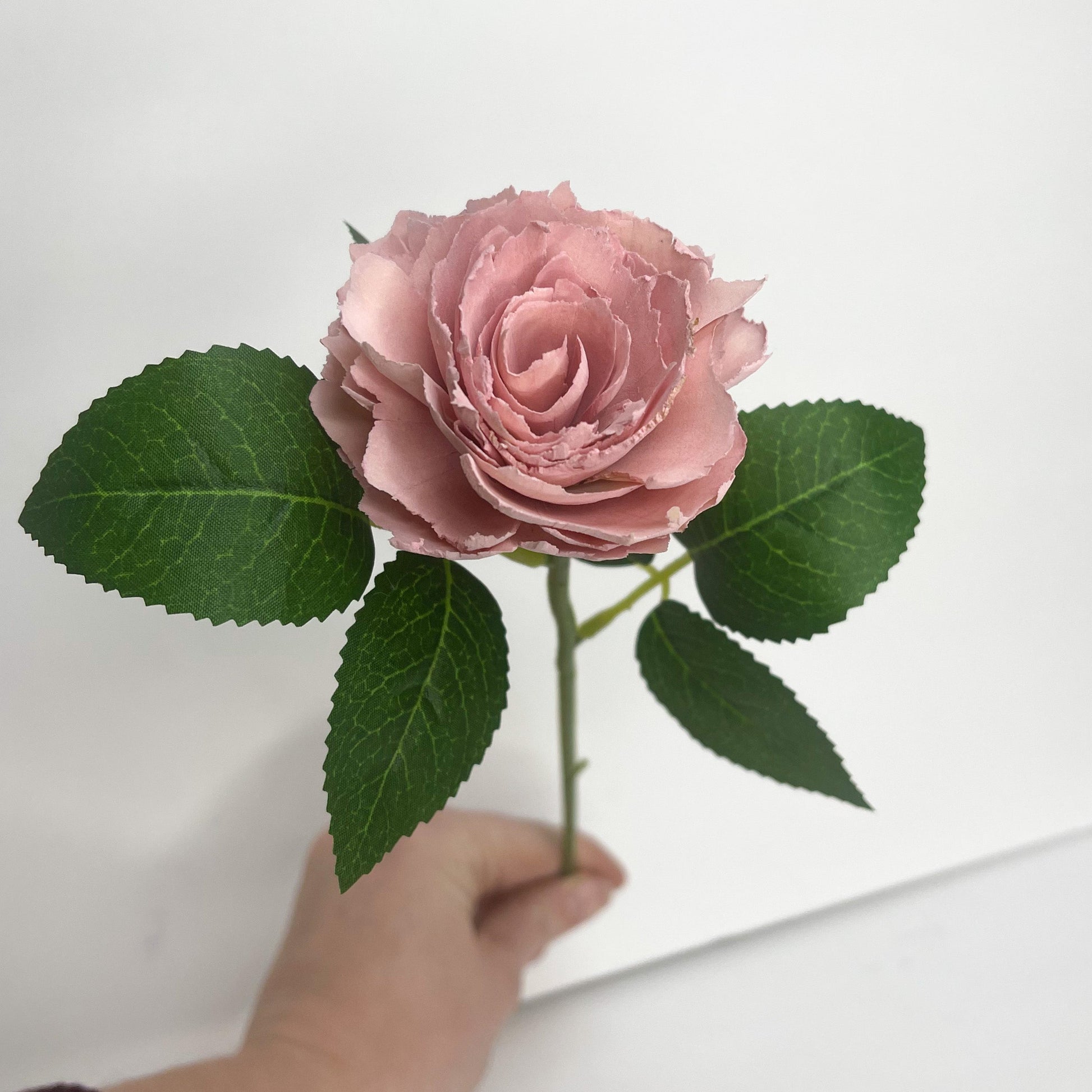 Single stem pink ruffled wooden rose with green leaves.