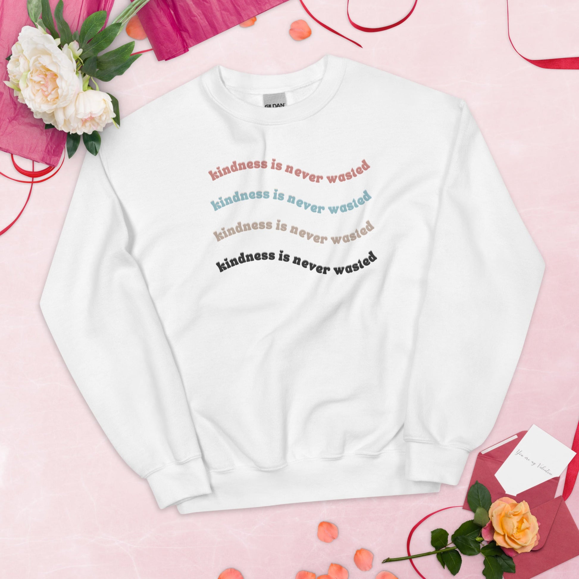 White "kindness is never wasted" crew neck with print in pink, tan, light blue, and black.